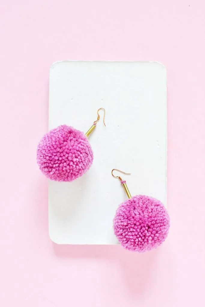 pink poofy pom pom earrings on white tray with pink background
