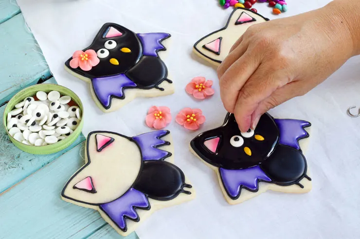 person putting eyes on bat shaped halloween cookies
